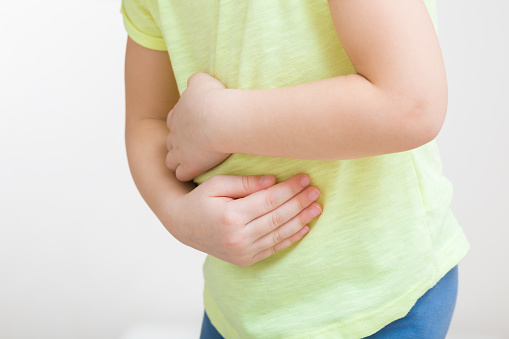 Little girl touching painful belly with arms isolated on light gray background. Closeup. Side view. Child suffering from stomach ache.