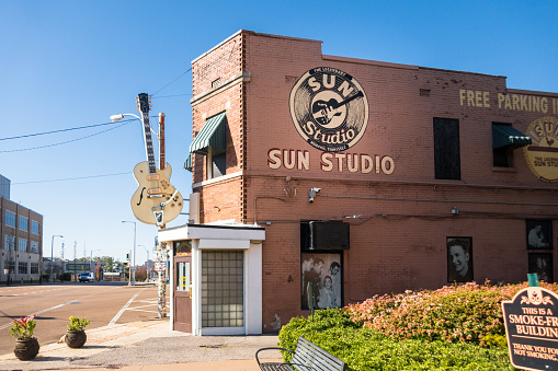 Exterior Sun Studios, Memphis, Tennessee, at mid-day, bright sunshine, bright blue sky, showing entrance from the side with Sun logo, large guitar, sidewalk.