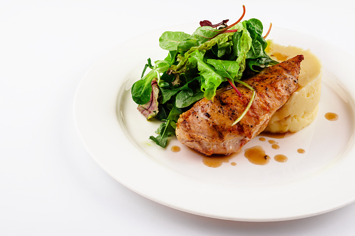 A white dish of chicken breast grilled with french fried and fresh dressing salad