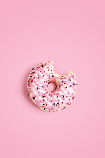 Sweet bitten donut on pink background. Color card. Creative layout. Tasty eating and sweet food concept. Top view, flat lay. Design element