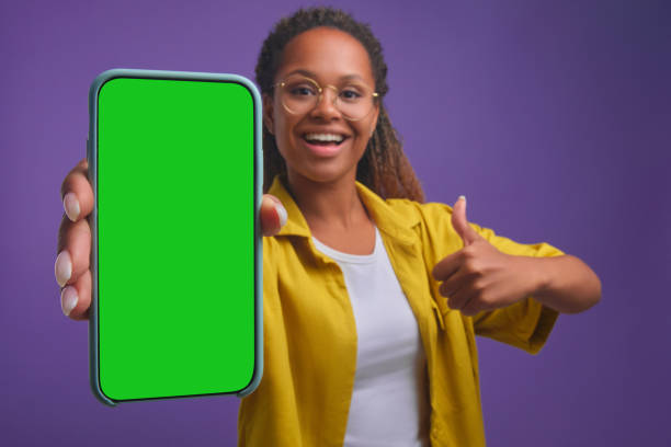 mulher afro-americana feliz nova com telefone de tela verde e mostra polegares para cima - chroma key fotos - fotografias e filmes do acervo