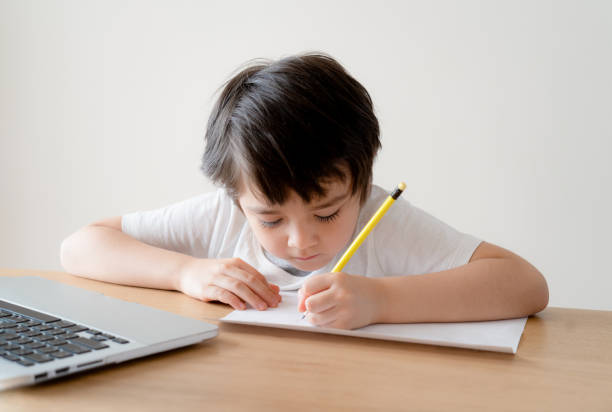 istock Primary school child boy learning writing doing homework sitting at home,Portrait preschool kid studying online making note with pencil using computer for his homework,Education and Technology concept 1461066522