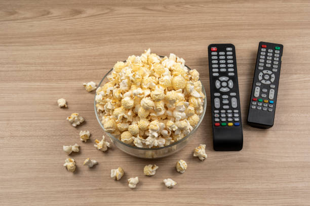 istock Popcorn in a glass bowl on wooden table and TV remote control 1461067017