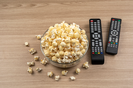 Popcorn in a glass bowl on wooden table and TV remote control