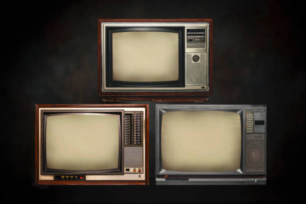 istock Three old-fashioned TVs with empty screens stacked in dark. Retro old television set pile on black background. 1461067244