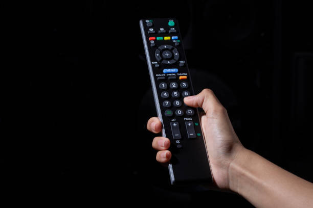 istock Woman hand holding TV remote control on black background 1461067256