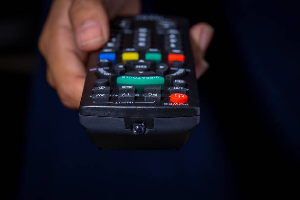 istock Woman hand holding TV remote control in dark background. Selective focus image 1461067260