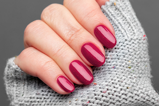 Female hand with beautiful manicure - viva magenta, burgundy glittered nails