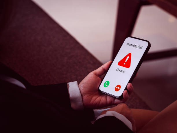 istock Incoming call with unknown caller, malicious phone calls concept. Red warning icon displayed showing on smart mobile phone in business person hand. Spam and robocalls, scam call alert, red tone. 1461069193