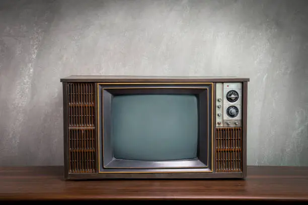 Photo of Close up photo of vintage old television on wood table in the room with concrete wall background.