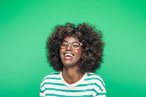 Headshot of excited afro american young woman wearing striped blouse, laughing at camera. Studio portrait on green background. Easter concept.