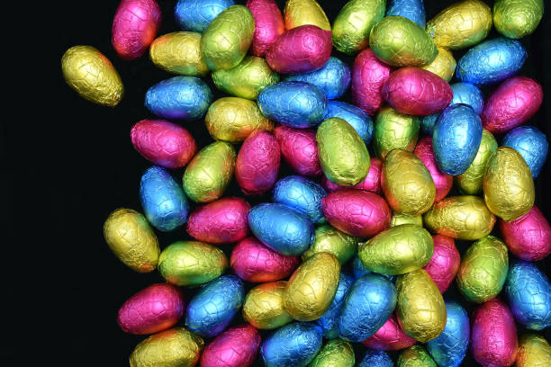 istock Pile or group of multi colored and different sizes of colourful foil wrapped chocolate easter eggs in pink, blue, yellow and lime green against a black background with copy space. 1461077620