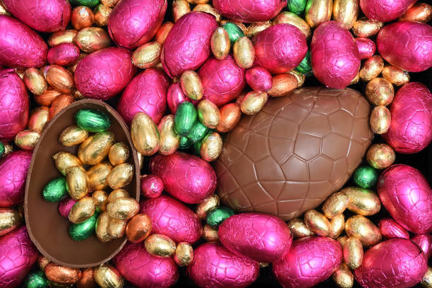 istock Pile or group of multi colored and different sizes of colourful foil wrapped chocolate easter eggs in pink, red, gold and lime green with two halves of a large brown milk chocolate egg in the middle. 1461077789