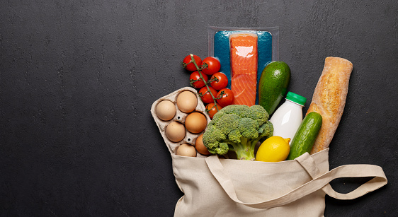 Shopping bag full of healthy food on stone background. Flat lay with copy space