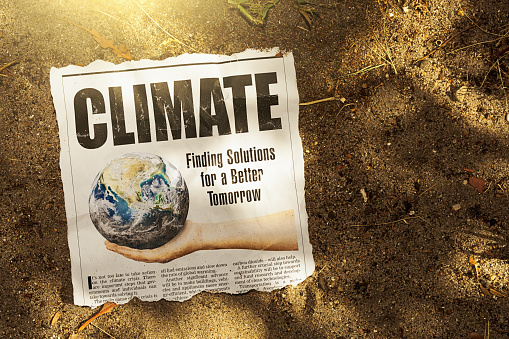 Newspaper clipping about solutions to the climate crisis lies in arid sand in bright sunlight, an image full of irony. Text was written from scratch by the photographer, who also did the design, so this image is free of third-party copyright and may be used without restriction. Public domain satellite Earth image from https://www.nasa.gov/multimedia/imagegallery/image_feature_2159.html