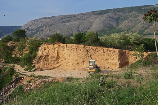 Recycling concrete and construction waste from demolition. Excavator at landfill of the disposa. Reuse of building rubble. Backhoe dig gravel at mining quarry on sunset background.