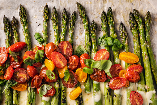 Remove the last few woody centimetres of the asparagus stalk, place on lined baking tray with the halved tomatoes, drizzle with olive oil and season with salt and pepper and bake at 180C/375F for 8-12 minutes. For the last couple of minutes cooking time add the shredded mozzarella to melt over the asparagus. Before serving, mix the tomatoes with the asparagus and melted cheese and add some fresh basil leaves. Colour, horizontal with some copy space.