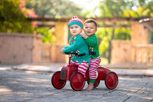 Cousins dress as Santa's elves driving a red car toy