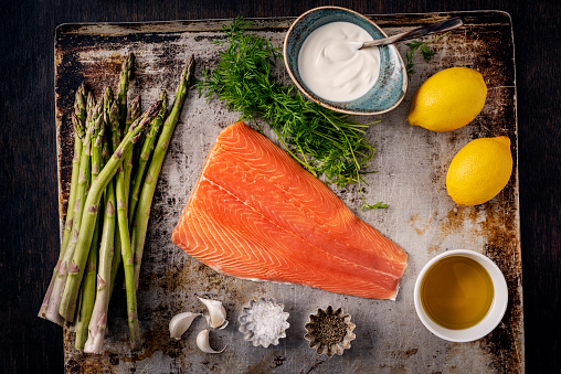 Flat lay view of all the ingredients you need to make asparagus with baked salmon. You will need, salmon,fresh asparagus, lemon juice, dill, olive oil, garlic, seasoning and yoghurt. Colour, horizontal with some copy space.