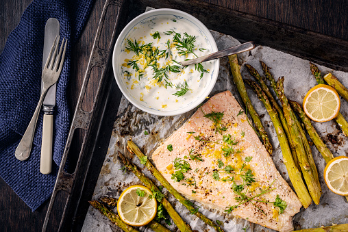 Baked salmon with asparagus with a yoghurt based dill and lemon flavoured dressing. You will need, salmon, fresh asparagus, lemon juice, dill, olive oil, garlic, seasoning and yoghurt. Colour, horizontal with some copy space. Bake 108C/375/F  for around 15 minutes.