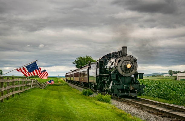 istock American Flags are Waving in the Wind, on a Fence, While a Steam Passenger Train Approaches 1461087826