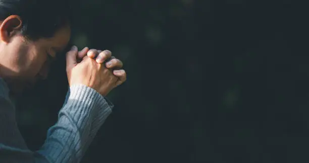 Photo of Christ religion and christianity worship or pray concept. Christian catholic woman are praying to god in dark at church. Prayer person hand in black background. Girl believe and faith in jesus