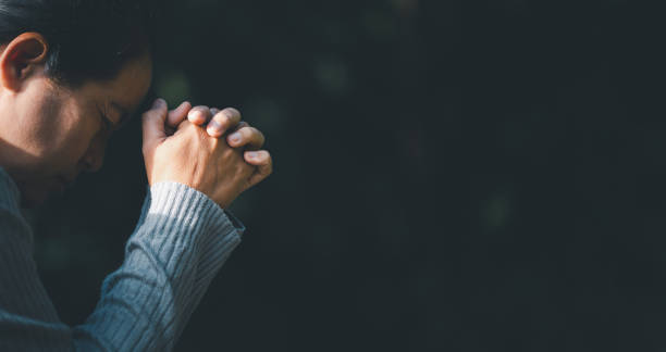 christ religion and christianity worship or pray concept. christian catholic woman are praying to god in dark at church. prayer person hand in black background. girl believe and faith in jesus - rezando imagens e fotografias de stock