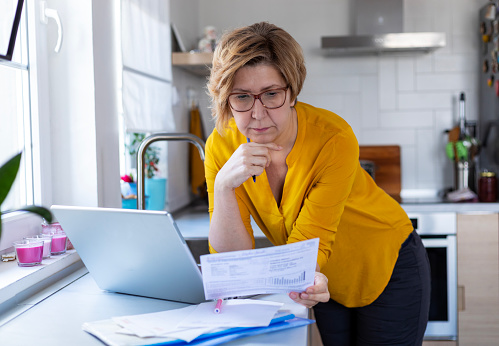 Concentrated mature woman calculating finance, money, using laptop computer at home , counting budget, paying bills, taxes, rent, mortgage fees