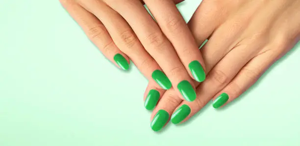 Beautiful groomed woman's hands with green nails on the light green background.