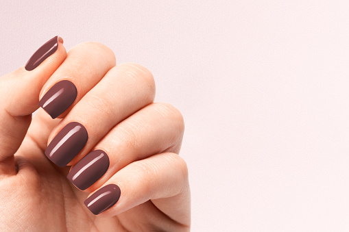 Female hands with brown nail design. Brown nail polish manicure on brown background. Nail design copy space.