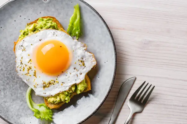 Avocado toast with fried egg on wooden table close up. Toasted bread with avocado and egg for healthy breakfast.