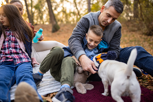 Mother and father with two kids and dog relaxing on blanket together in nature on autumn day.