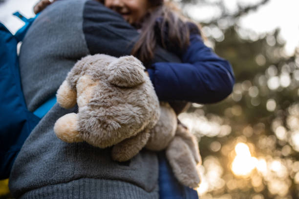 Father holding his daughter in arms, while she is holding her favorite toy in nature on autumn day.