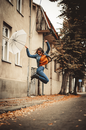 Beautiful young woman jumping with an umbrella outdoors in autumn.