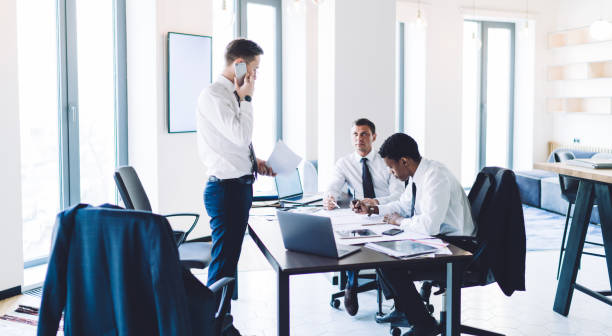 istock Businessman with papers standing and phoning while working with multiethnic colleagues in office 1461109530
