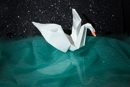 White paper origami swan on green dark background, soft focus close up