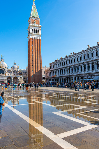 Doge's palace and Campanile on Piazza di San Marco, Venice, Italy with sea water on foreground. Calm sunny day in Summer, blue sky with clouds.