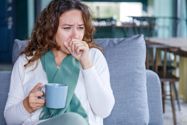 istock Young woman sitting on sofa and having cough while suffering from sore throat 1461112995