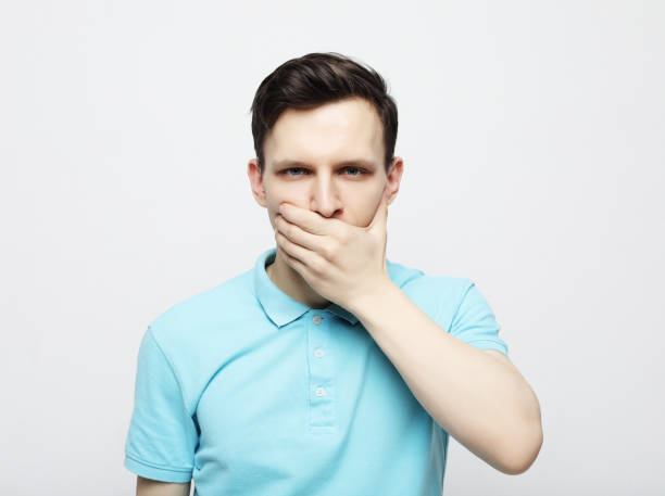 istock A young man dressed in a blue shirt covers his mouth with his palms. 1461114227