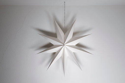 Cardboard paper star hanging on a white wall background. Simple nordic style home festive geometric decoration, christmas, winter time.