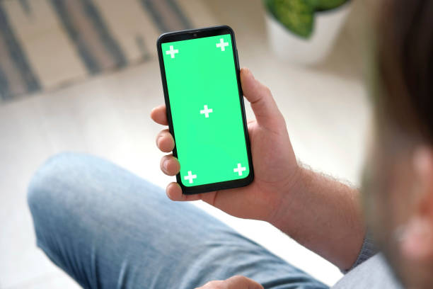 Young man sitting at home holding smartphone green mock-up screen in hand. Male person using chroma key mobile phone. Vertical mode. Touching, swiping display, tapping, surfing Internet social media. Caucasian Man finger clicking, tapping and swiping on center of chromakey green screen. Handsome guy using phone mockup. Close up. Footage Pack. Using for a smartphone, tablet pc or a touch screen devices. Gestures. cellphone with tracking markers. watching content joven sentado en casa sosteniendo una pantalla de maqueta verde de teléfono inteligente en la mano. persona masculina usando el teléfono móvil chroma key. modo vertical. tocar, deslizar la pantalla, tocar, navegar por las redes sociales de internet