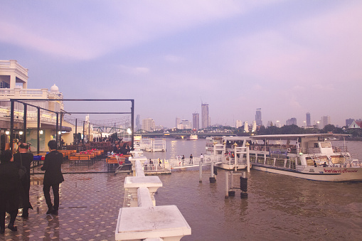 Yodpiman Riverwalk promenade and pier in Bangkok  at sunset of after rain. A few thai people are in scene. They are dressed in black at day of funeral of King Rama IX.  Promenade is seated near Buddhayodfa Chulalok Maharat Bridge and has pier for passenger boats named Yodpiman 2 pier.