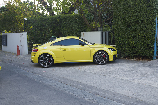 Parked yellow Audi TT RS in front of hedge in street in residential district of Bangkok Chatuchak