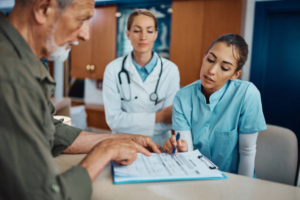 Young need to write your personal data right here! Young nurse assisting senior man to fill out medical documents at reception desk at doctor's office. medical clinic stock pictures, royalty-free photos & images