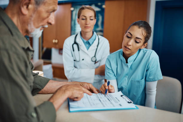 Young need to write your personal data right here! Young nurse assisting senior man to fill out medical documents at reception desk at doctor's office. clinic stock pictures, royalty-free photos & images