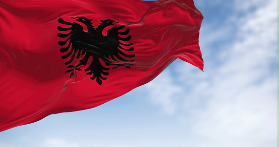Close-up view of the Albanian national flag waving in the wind. Red flag with black two-headed eagle. Fabric textured background. Selective focus