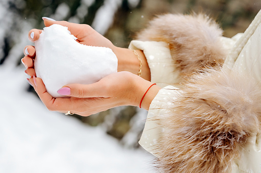Hands of young woman holding heart- shaped snow