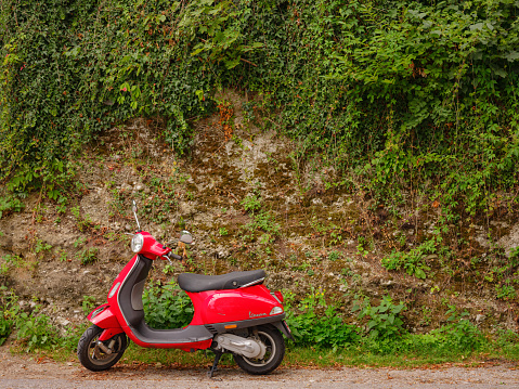 Munich, Germany - August 4, 2022 : personal transport, a beautiful red Vespa moped stands near a green wall in the city