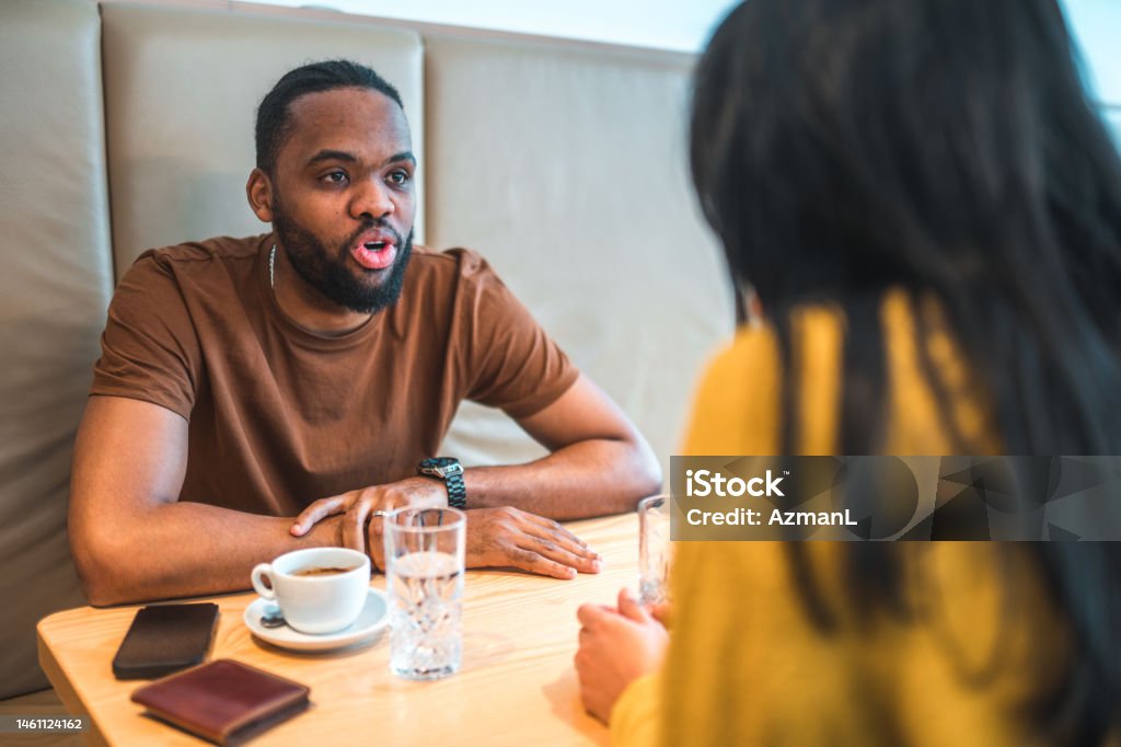 Mid Adult Biracial Mixed Couple Sitting at Lunch Waist up shot of a mid adult  African-American  man , sitting at the table with a black-haired woman, having coffee and water while talking. Smart phone and wallet on the table. 30-34 Years Stock Photo
