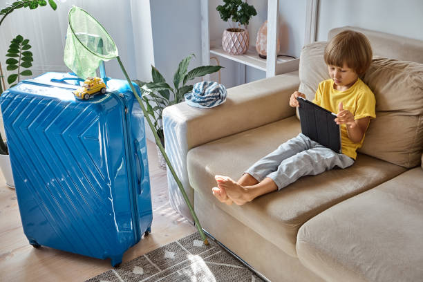 istock Child using a tablet buying online tickets or waiting for vacation at home next to a packed suitcase 1461125196